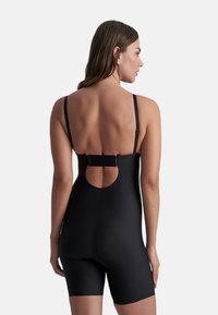 Trikini negro con corte en la espalda, tirantes ajustables y estilo de pantalones cortos. Fabricado con material suave y elástico. Cuenta con un cierre de gancho.