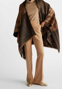 Hnědý pončo se pruhy a třásněmi, nošené přes béžový top a spojené s béžovými rozšířenými kalhotami a zlatými mokasínami.