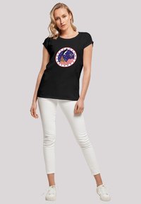Black cotton t-shirt with short sleeves, featuring a circular graphic of a ship on a blue background with red and white stripes and stars.