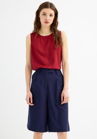 Top sin mangas en color burdeos combinado con pantalones culottes de tiro alto en color marino. Tejido suave, corte holgado, con pliegues en la parte delantera y bolsillos laterales en los pantalones.