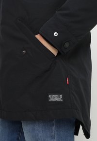 Veste noire avec poignet boutonné et poche latérale. Présente une étiquette Levi's à l'ourlet. Fabriquée en tissu texturé, conçue pour la chaleur et la fonctionnalité.