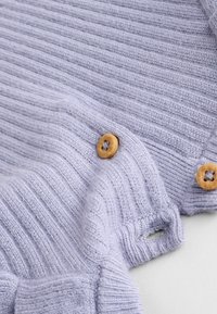 Vaaleanvioletti neulottu neule, jossa on ribbikuvio ja puunappikoristeet. Koostumuksessa on pieniä aukkoja nappien lähellä.