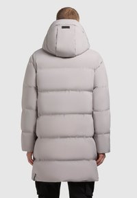 Gai pelēks pūkains mētelis ar kapuci, ar quiltēta dizainu, garām piedurknēm un nedaudz pagarinātu griezumu. Ietver nelielu logo detaļu.