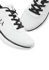 Weiße Sportschuhe mit einem strukturierten Strickoberteil, schwarzer Schnürung und einem schwarzen Akzent entlang der Sohle, mit einem runden Zehendesign.