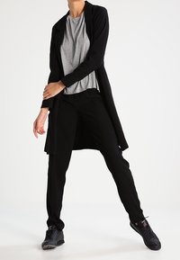 Czarny długi kardigan na szarym T-shircie, zestawiony z czarnymi spodniami i czarnymi trampkami. Gładka tkanina z minimalnymi zdobieniami.