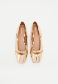 Bailarinas doradas con un acabado metálico brillante; punta redonda; parte superior de tejido suave; ribete elástico; pequeño detalle de lazo en la parte frontal.