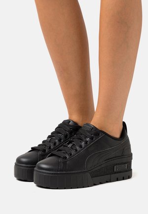 Czarne sneakersy na platformie z gładkiej skóry, zaokrąglonym noskiem, grubą teksturowaną podeszwą i sznurowanym przodem z widocznym logo.