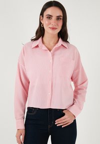 Pink and white striped button-up shirt with a collar, long sleeves, and a single chest pocket, made from textured fabric.