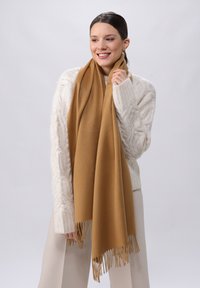 pruun villane sall, millel on 짧ированные края, vabalt riputatud, creemivärvi nööriga kootud sviitri kõrval. Lihtne, elegantne disain.