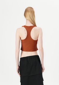 Top corto marrón con escote redondeado y grandes agujeros para los brazos, combinado con una falda con cinturilla elástica negra. Textura de tela suave.