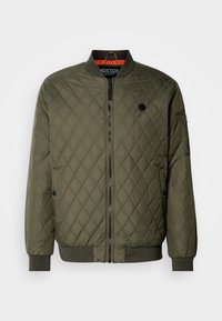 Veste bomber matelassée vert olive avec une fermeture éclair noire, des poignets côtelés et une doublure orange contrastante. Présente des poches latérales et un accent logo.