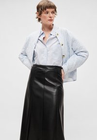 Világoskék steppelt dzseki függőleges fehér csíkokkal, fekete bőr ceruzaszoknyával párosítva, mely elülső varrásokkal rendelkezik.