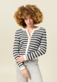 Cárdigan a rayas en negro y blanco de punto con un cuello y botones en crema; cuenta con mangas largas y un diseño ajustado.