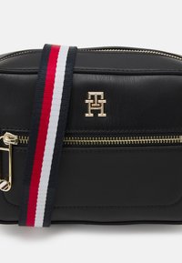 Borsa a tracolla in pelle nera con una cerniera dorata, logo brandizzato e cinturino a righe nei colori blu, rosso e bianco.