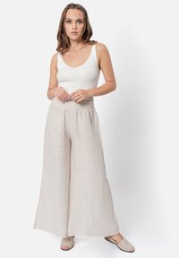 Pantaloni in lino leggeri e fluidi di un morbido colore beige con una vita elasticizzata, abbinati a un top aderente bianco a coste e sandali scivolati beige.