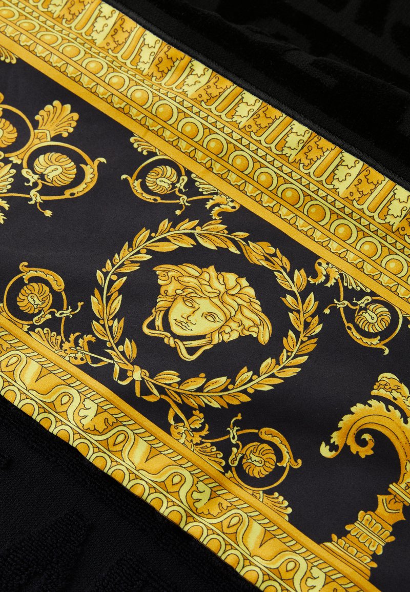 Schwarzer Stoff mit kunstvollen goldenen Verzierungen, darunter ein zentrales Medaillon mit einem Gesicht, Blumenmustern und dekorativen Bordüren.