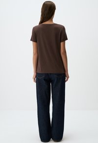 T-shirt marrone a maniche corte con scollo rotondo, abbinato a jeans in denim blu scuro dal taglio slouchy con tasche posteriori. Presenta una texture liscia.