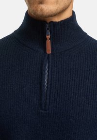 Mørkeblå halv-zip pullover lavet af struktureret strikstof, med en kontrasterende læder zip-hendel og ribbet krave.