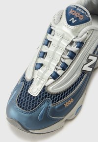 Baskets en maille bleue et en synthétique argenté avec des détails texturés, fermeture à lacets, languette rembourrée et un distinct logo "N" sur le côté.
