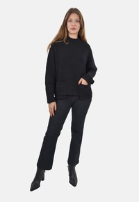 Maglione nero in maglia con collo alto, due tasche frontali e polsini a coste, abbinato a jeans scuri e stivaletti neri con tacco.