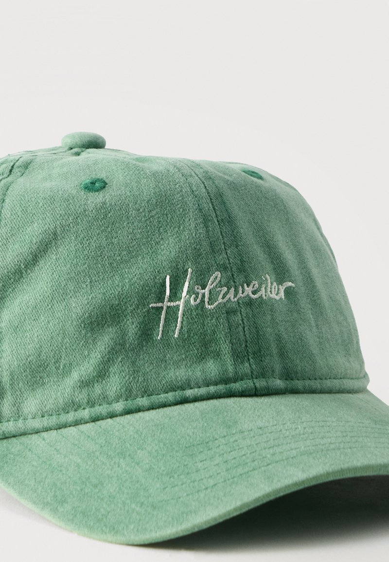 Grüne Baumwoll-Baseballkappe mit leicht gebogenem Schirm und "Holzweiler" in weißer Schrift auf dem Frontpanel bestickt.