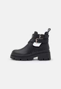 Botas negras hasta el tobillo con dos correas de hebilla, suela de plataforma gruesa y lados recortados, hechas de cuero suave con un acabado mate.