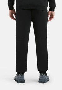 Zwarte sweatpants met een taperend ontwerp en elastische boorden, gecombineerd met grijze sneakers met gestructureerde zolen en subtiele merkdetails.