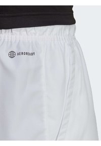 Närbild av vita shorts med elastisk midja med "AEROREADY"-logotyp och diskret sidoficka, bärs med en svart topp.