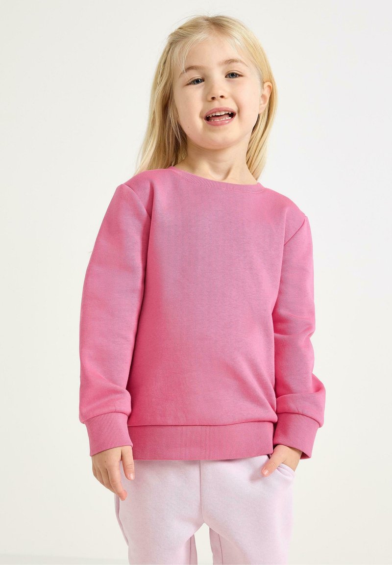Rosa Sweatshirt mit Rundhalsausschnitt und gerippten Bündchen. Aus weichem Stoff gefertigt, mit glatter Textur. Getragen mit hellrosa Jogginghosen.