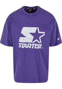 T-shirt en coton violet avec un grand graphique blanc fissuré de la lettre "S" et une étoile, avec "STARTER" imprimé en dessous. Manches courtes, coupe décontractée.