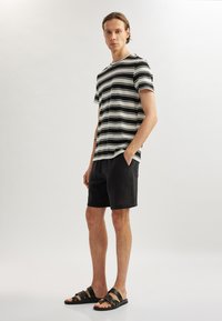 Sort-hvid stribet t-shirt med korte ærmer, parret med sorte strukturerede shorts og sorte sandaler med remme.