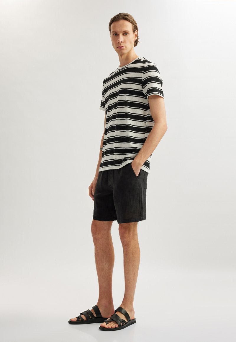Sort-hvid stribet t-shirt med korte ærmer, parret med sorte strukturerede shorts og sorte sandaler med remme.
