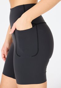 Shorts da ciclismo neri a vita alta realizzati in tessuto elasticizzato, con una tasca laterale e dettagli di cucitura a contrasto.