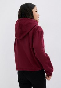 Hoodie borgogna, tagliato, con un ampio cappuccio e maniche lunghe. Tessuto morbido in cotone; design casual con dettagli di cucitura visibili.