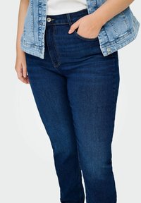 Tamsiai mėlynos džinsinės kelnės su lieknu siluetu, su standartiniu juosmeniu ir kišenėmis. Užsidėta su šviesiai mėlynu džinsiniu švarku.