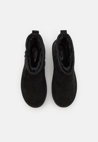 Une paire de bottines noires avec une doublure douce et duveteuse visible à l'intérieur, vue de dessus sur un fond blanc uni.