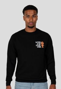 Zwarte sweatshirt met een graphic waarop staat "WRONG FRIENDS" met een oranje karakter. Het materiaal lijkt zacht, met een ronde hals en geribde manchetten.