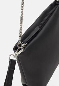 Černá kožená taška s hladkým povrchem, vyznačující se zipovým zapínáním, odnímatelným popruhem a stříbrným řetízkem jako akcentem.
