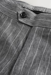 Tissu rayé gris avec un bouton noir, une ceinture détaillée et une doublure intérieure texturée. Les textiles semblent légers et respirants.