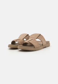Sandales en suède beige avec deux larges bandes croisées, une surface texturée et une semelle en caoutchouc plate. Design simple sans quincaillerie visible.