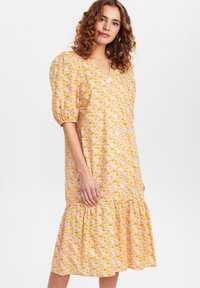 Vestido floral em amarelo, rosa e laranja; apresenta um decote em V, mangas bufantes, detalhes em botões e barra franzida; feito de tecido leve.