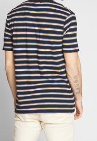 Kortærmet t-shirt i sort med smalle vandrette striber i blå, orange og hvid. Blødt stof med en afslappet pasform.