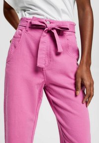 I pantaloni di cotone rosa presentano una vita con cintura, tasche laterali e una vestibilità ampia con una texture liscia.