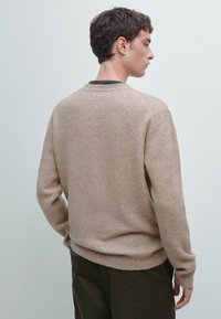 Maglione lavorato a maglia beige con scollatura rotonda, maniche lunghe e vestibilità comoda, caratterizzato da una superficie morbida e textured.