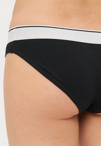 Funda preta de algodão com uma faixa elástica branca com uma risca preta. A funda tem uma textura suave e um cortestandard.