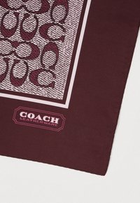 Écharpe carrée en soie bordeaux avec un motif géométrique en rose et blanc, arborant un logo "COACH Leatherware" dans le coin inférieur.