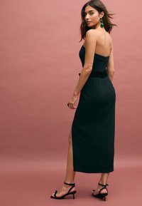 Rochie neagră fără bretele, cu un corset ajustat, curea din catifea și o fante pe o parte. Pur și simplu cu sandale negre cu toc și cercei verzi statement.