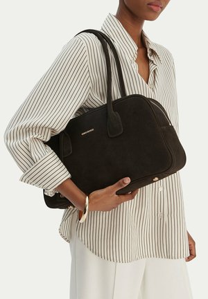 Persona che indossa una camicia a righe con bottoni e tiene una borsa nera GINO ROSSI con doppi manici e un braccialetto dorato al polso.