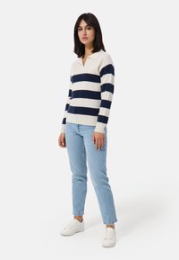 Pullover a righe blu navy e bianche in maglia con colletto polo. Abbinato a jeans azzurri chiari e sneakers bianche. Texture liscia, vestibilità comoda.