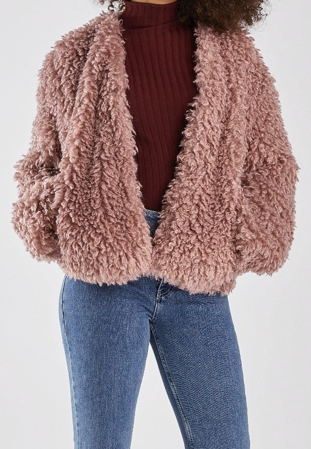 Luddig, kort kappa i ljusrosa, med en mjuk textur, överdimensionerade ärmar och en öppen frontdesign. Kombinerad med en ribbad vinröd topp och denimjeans.